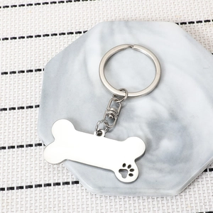 Polished stainless steel bone shaped keychain with hollow paw print on marble tray