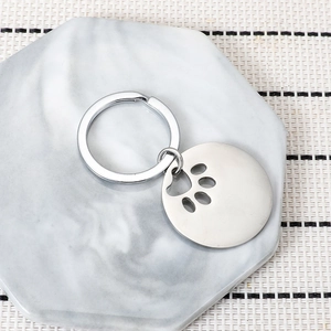 Polished stainless steel dog tag keychain with animal paw cutout on marble background