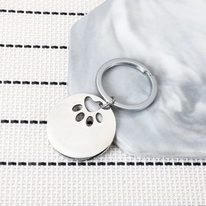Polished stainless steel pet ID tag with hollow dog paw cutout on marble background