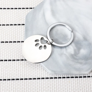 Minimalist silver stainless steel dog tag keychain with hollow paw print on marble tray