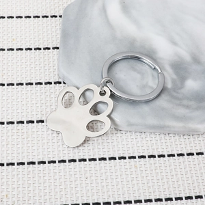 Polished stainless steel cat paw keychain with hollow design on marble coaster