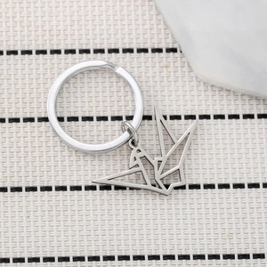 Polished stainless steel origami crane keychain with a geometric hollow design on a woven mat