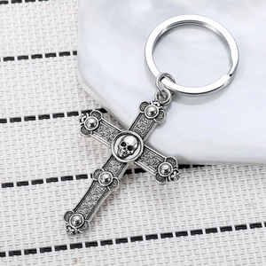 Vintage silver skull cross keychain with intricate embossed details on white textured mat