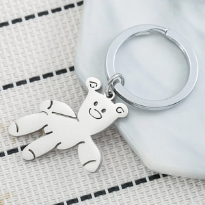 Polished stainless steel teddy bear keychain on a modern marble tray background