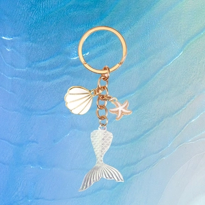 Mermaid tail keychain with iridescent charm, white shell, and starfish on blue wave background