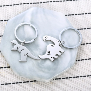 Matching stainless steel dinosaur couple keychains with heart cutouts on marble tray