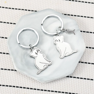 Set of two cute cartoon cat stainless steel keychains on marble tray, stylish bag charms