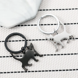 Minimalist cat keychains in black and silver finish on a textured white surface