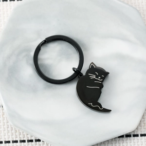 Cute black magnetic cartoon cat keychain made of metal on a white marble display tray