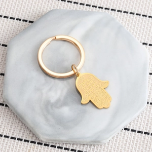 Golden Hamsa hand stainless steel keychain on marble tray with Hebrew engraving