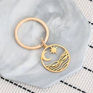 Minimalist gold stainless steel keychain with hollow star moon and wave pendant on marble
