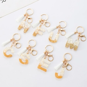 Resin alphabet keychain set with white stones, gold leaf, and tassel on white background