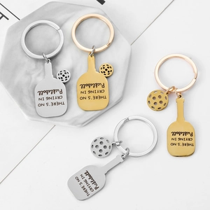 Golden and silver stainless steel pickleball racket keychains set on marble background