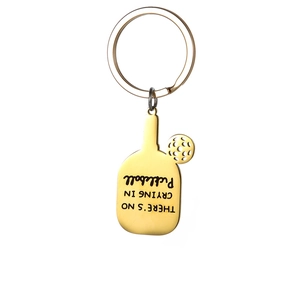 Macro view of golden pickleball paddle and hollow ball keychain with polished finish