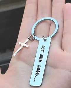 Polished silver stainless steel cross keychain with engraved text held in hand for scale
