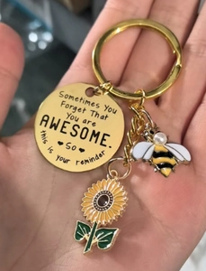 Detail showing bee and sunflower charms with inspirational quote on gold keychain