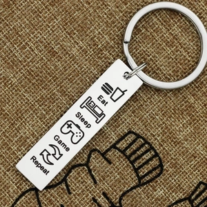 Macro detail of stainless steel keychain with Eat Sleep Game Repeat engraved icons