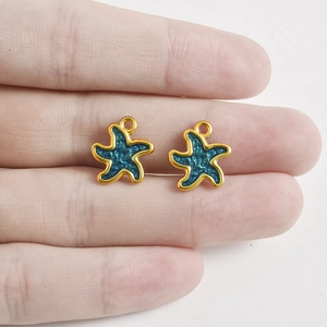 Nahaufnahme von 18k vergoldeten Seestern-Anhängern mit blauem Emaille auf einer Hand