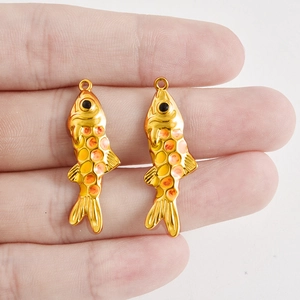 Detail von kleinen Goldfisch-Anhängern mit gelber Emaille auf den Fingern