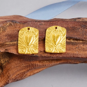 Detail showing two gold heart engraved rectangular pendants with scroll patterns on wood