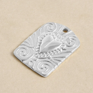 Detail of silver heart-stamped pendant with ornate scrollwork texture for jewelry making