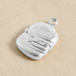 Detailed close-up of a silver burger-shaped metal pendant with intricate sesame texture