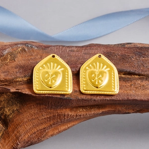 Detail of 18k gold-plated heart shield charms with snowflake texture on dark wood background