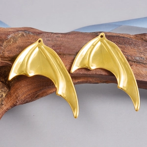 Macro shot of gold-plated bat wing pendants on driftwood for DIY jewelry making
