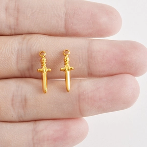 Pendentifs épée en acier inoxydable doré pour bijoux DIY présentés sur une main