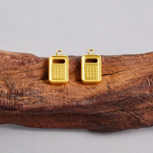Macro detail of two golden stainless steel calculator pendants on natural tree bark background