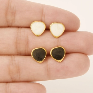 Set of black and cream heart enamel stud earrings with gold plating shown on hand