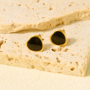 Elegant stainless steel heart earrings in gold and black on a textured beige stone display