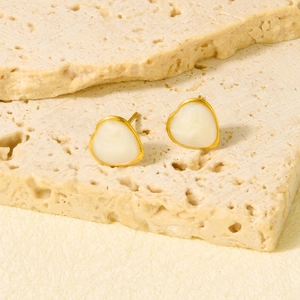 Detail of gold heart earrings with white enamel inlay on a rustic stone background