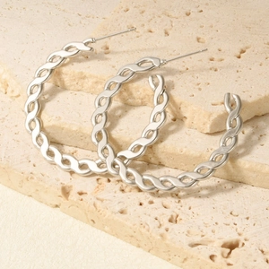 Detail of large silver twisted woven chain hoop earrings on travertine stone