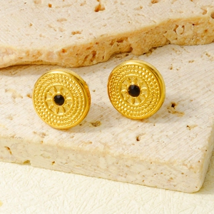 Macro shot of gold sunburst earrings with black stone on a travertine stone surface