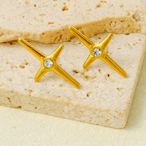 Gros plan de boucles d'oreilles croix dorées avec zircon brillant sur fond de pierre
