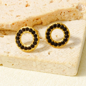 Elegant minimalist hollow round gold earrings with black inlaid stones on stone background