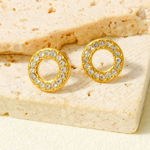 Close-up of golden hollow round stud earrings with sparkling crystals on stone texture