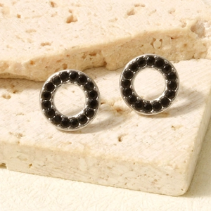 Close-up of silver hollow circle earrings with micro-pave black stones on stone surface