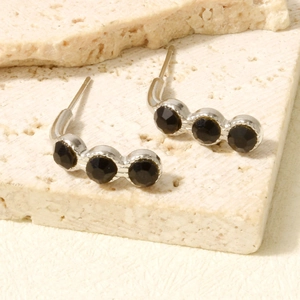 Detailed close-up of silver-tone ear crawlers with three black stones on a stone base