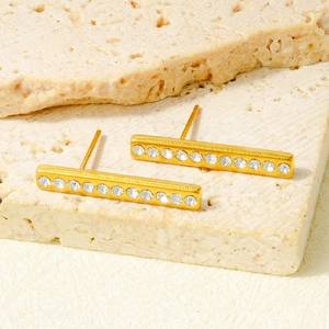 Dettaglio degli orecchini a barra dorati con cristalli micro-pavé su supporto in pietra