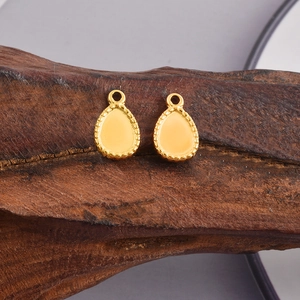 Macro view of gold teardrop pendants with milgrain edges on a dark wood block