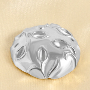 Macro view of silver leaf embossed stainless steel charm with metallic texture on satin