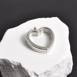 Macro detail of heart-shaped stainless steel locket with inset crystals on white rock