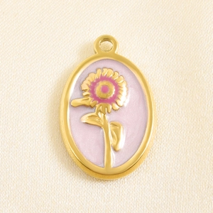 Detailed macro of oval sunflower enamel pendant charm with golden frame on silk background