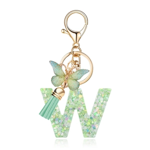 Green resin letter W keychain with butterfly charm and sequins on a white background