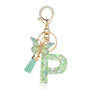 Macro detail of resin letter P keychain with green sequins, butterfly charm and silk tassel