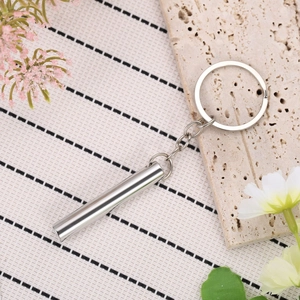 Minimalist silver steel cylinder whistle keychain on a warm decorative desk setting