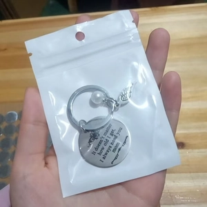 Macro detail of silver mother keychain with pearl and feather charms in poly bag