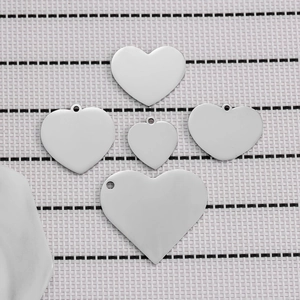 Polished stainless steel heart-shaped pendants in five sizes on a plaid background